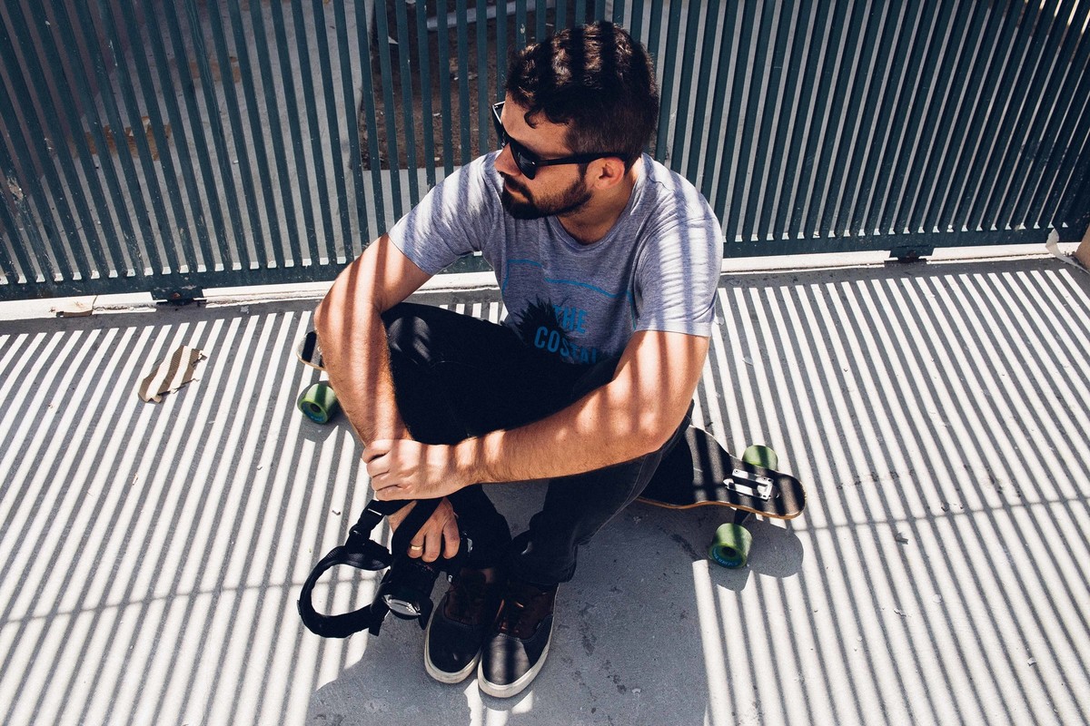 Ensaio masculino em Betim MG em que o modelo esta sentado encima de um longboard olhando para o lado