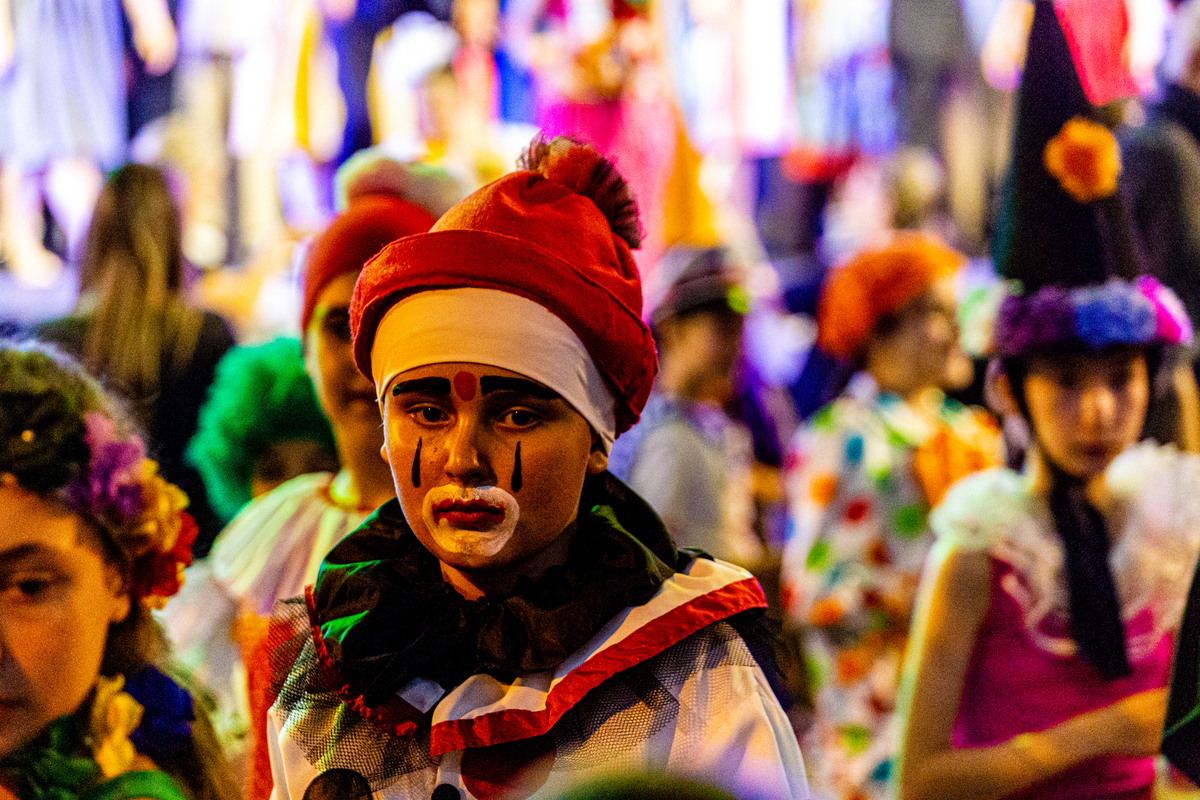 Menino fantasiado de palhaço, triste na multidão. 