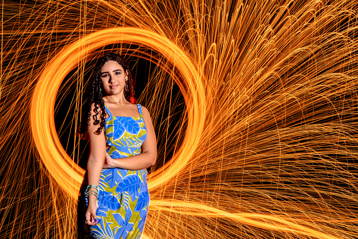 Debutante sorrindo durante ensaio de 15 anos na praia com iluminação feita com bombril incandescente ao fundo, Rio de Janeiro - RJ
