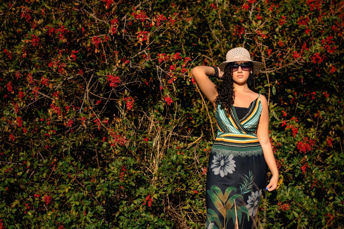 debutante com óculos escuros e chapéu com flores vermelhas ao fundo