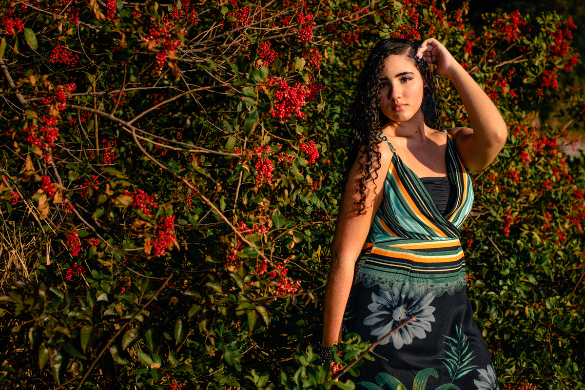debutante coma mão no cabelo, olhando para a câmera, com flores vermelhas ao fundo, Camboinhas - Niterói