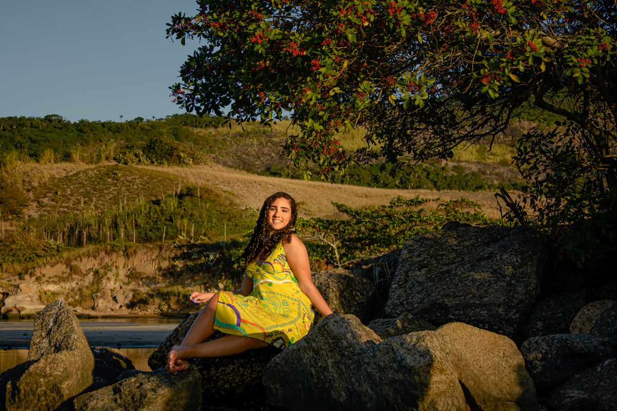 debutante sentada na pedra com árvore com flores vermelhas no canal de Itaipú, Camboinhas - Niterói - RJ