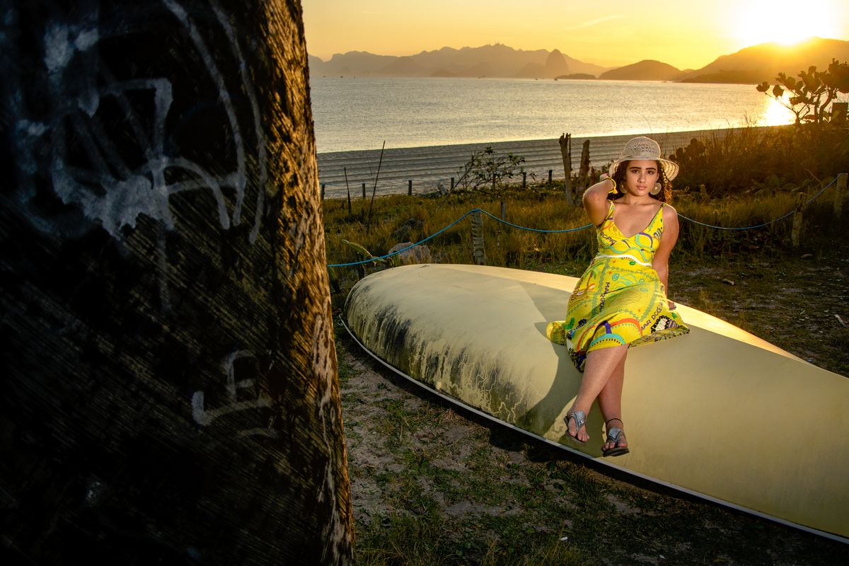 Debutante sentada no barco com a mão no chapéu ao por do sol na praia, Rio de Janeiro - RJ