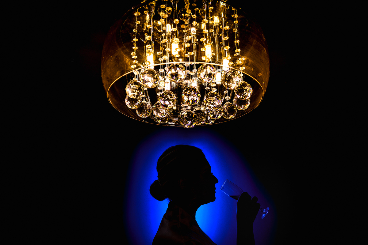 noiva bebendo champagne em baixo do lustre com luz azul atrás