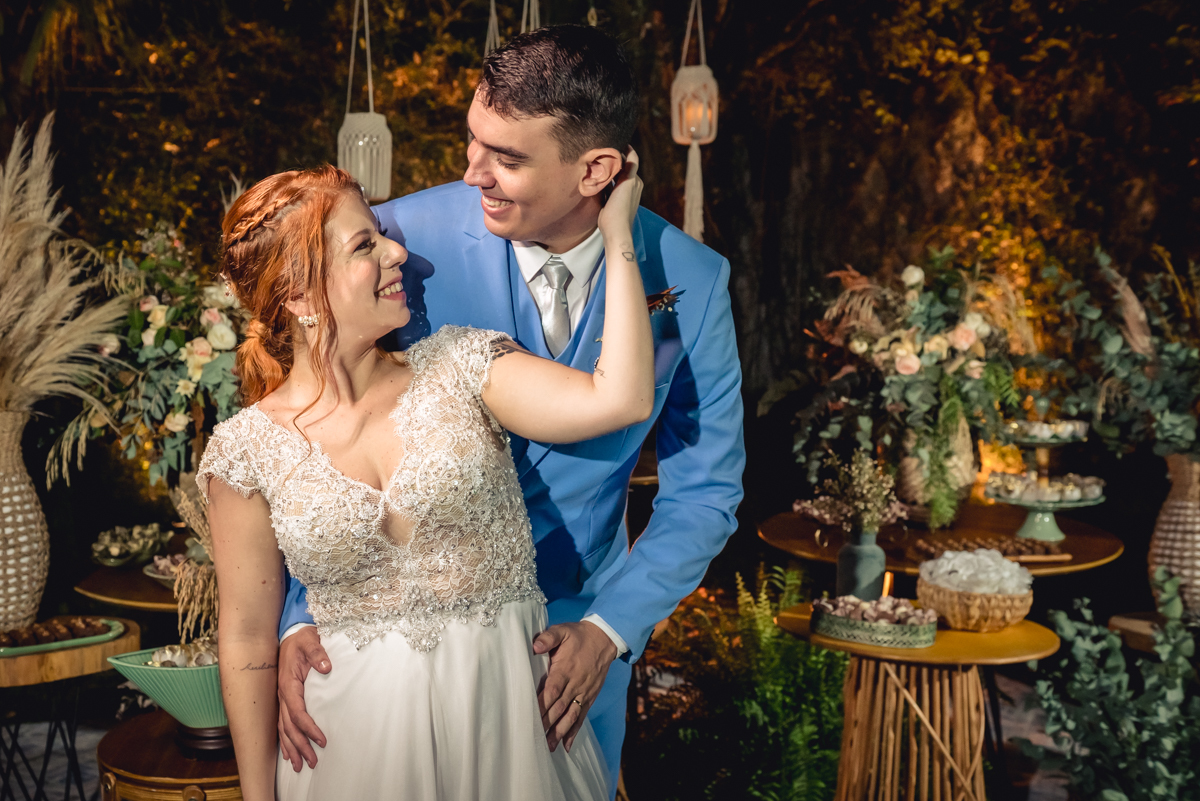 noivos abraçados e se olhando com a decoração da mesa do bolo ao fundo no casamento no campo no sitio na barra da tijuca - RJ