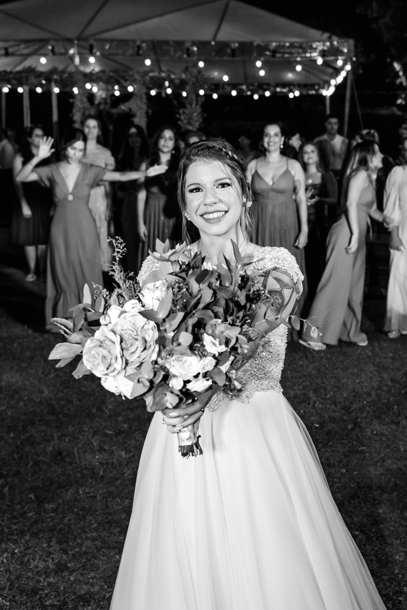 noiva em preto e branco preparada para jogar o buquê com convidados ao fundo na recepção na festa de casamento no campo no sitio na barra da tijuca - RJ