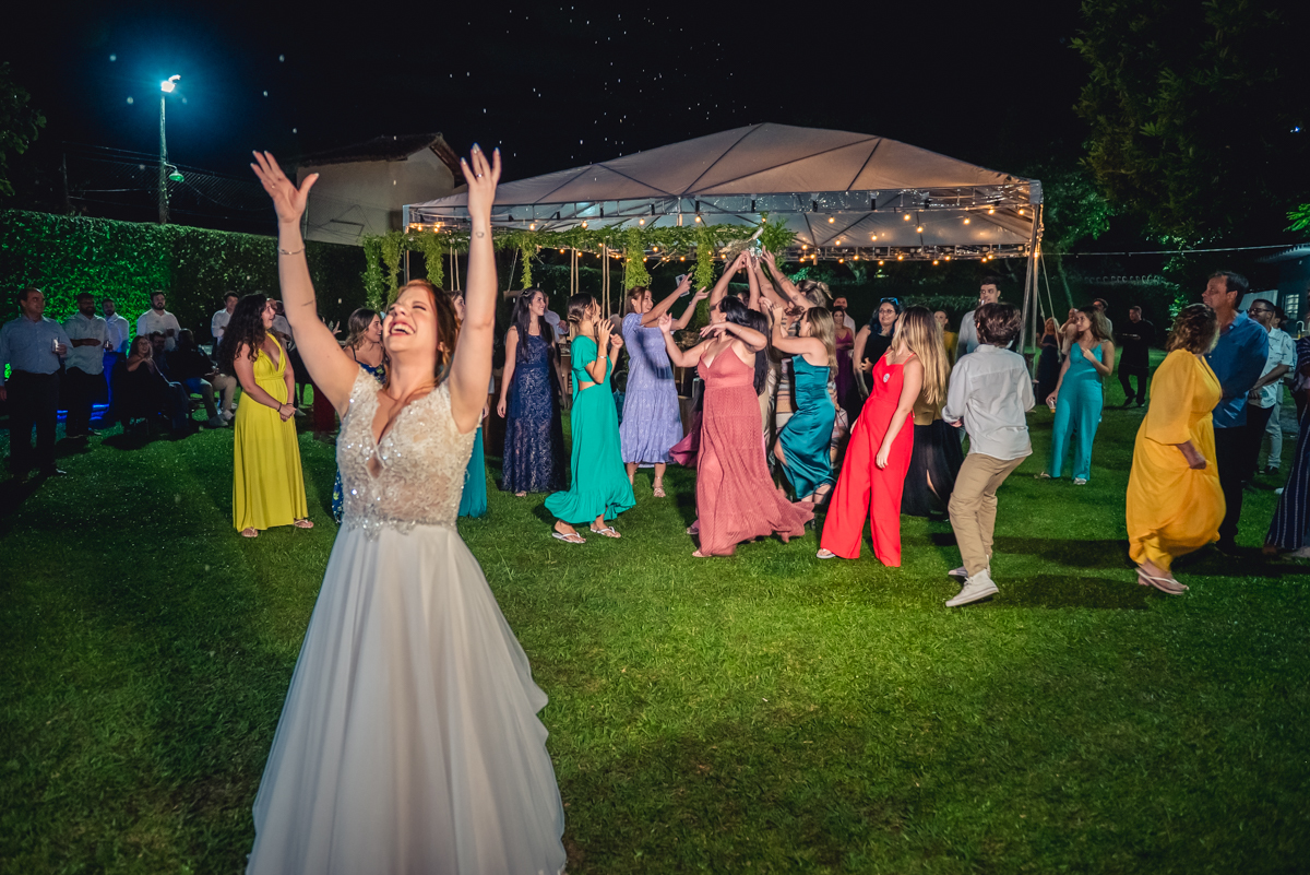 noiva jogando o buquê com convidados ao fundo na recepção na festa de casamento no campo no sitio na barra da tijuca - RJ