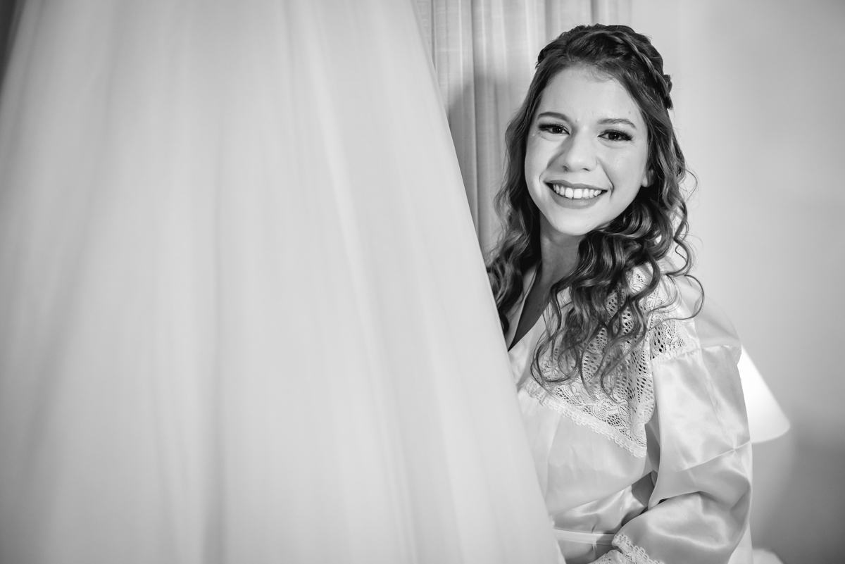 fotografia em preto e branco da noiva caroll sorrindo ao lado do seu vestido de casamento durante o making of no hotel Wyndham rio barra - RJ