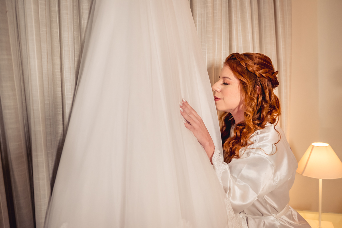 fotografia da noiva caroll contemplando o seu vestido de casamento durante o making of no hotel Wyndham rio barra - RJ