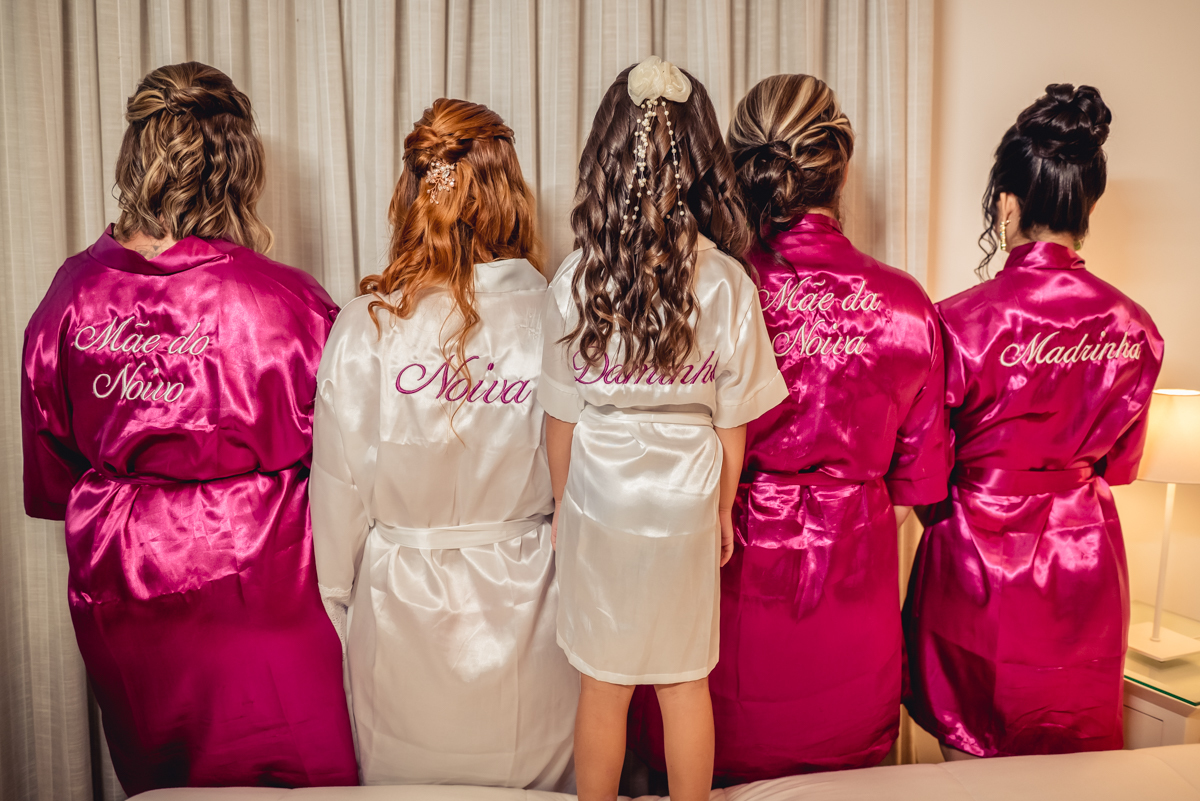 fotografia da noiva com madrinhas, daminha e sua mãe de costas com nomes nos robes durante o making of no hotel Wyndham rio barra - RJ