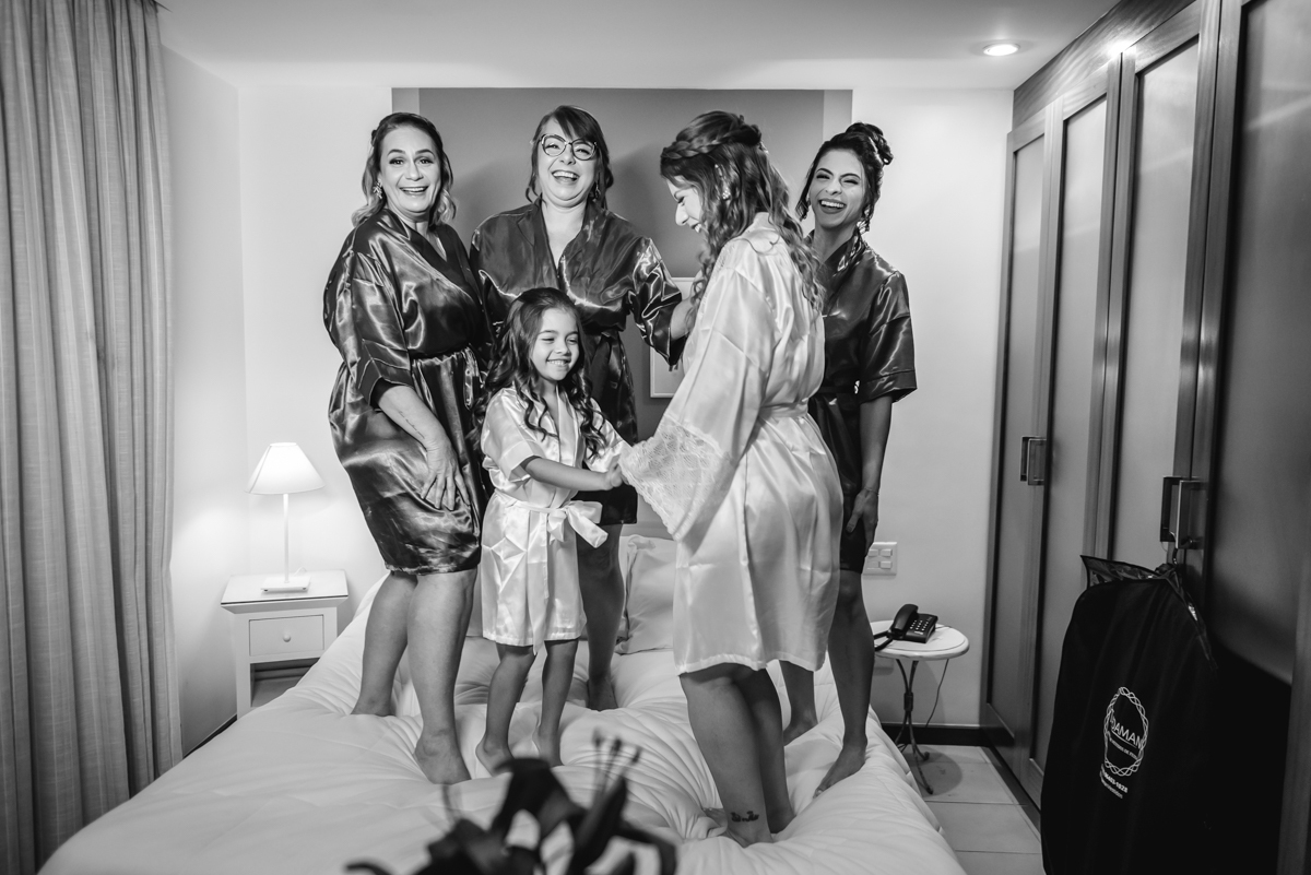 fotografia em preto e branco da noiva com as madrinhas pulando na cama no hotel barra - RJ