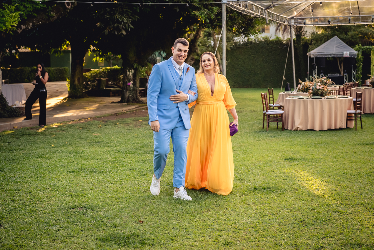 Entrada do noivo com terno azul e sua mãe com vestido amarelo no gramado verde para a cerimonia de casamento no sitio da paz, Barra da Tijuca - RJ