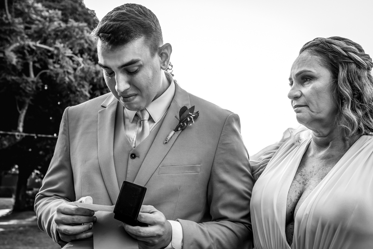 Fotografia em preto e branco do noivo emocionado ao receber a lembrança com a foto da irmã falecida na entrada da sua cerimonia de casamento no sitio da paz, Barra da Tijuca - RJ