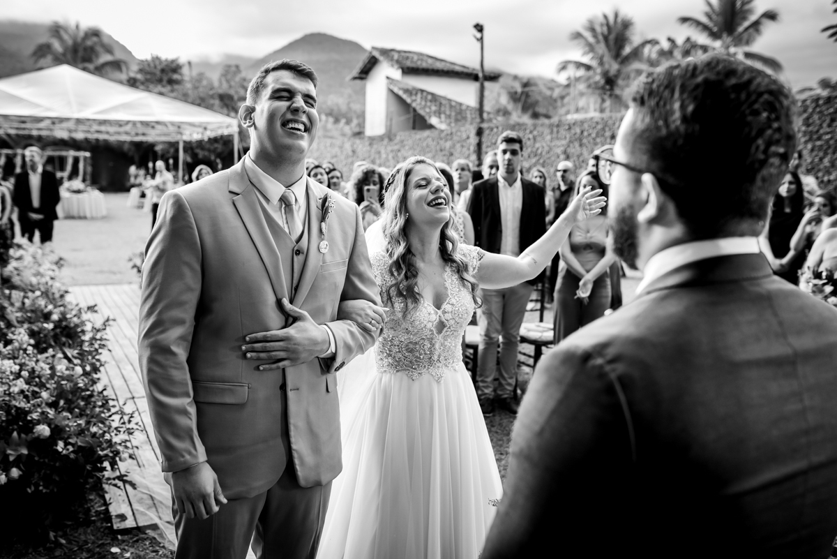 fotografia em preto e branco dos noivos sorrindo e cantando louvor em frente ao pastor na cerimonia de casamento no sitio da paz na barra da tijuca