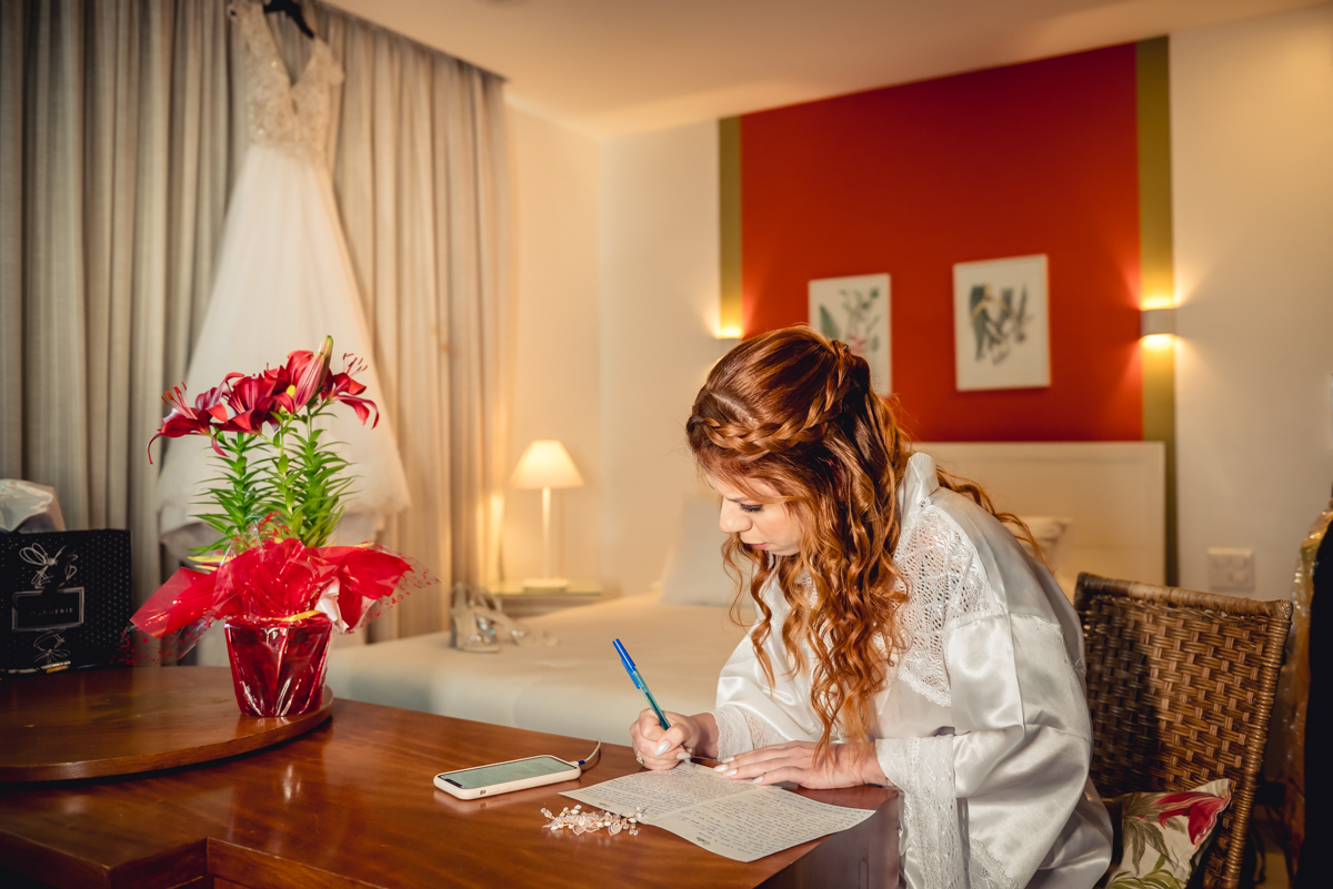 noiva escrevendo o depoimento com o vestido de casamento ao fundo no quarto do hotel durante o making of no hotel Wyndham rio Barra na barra da Tijuca - RJ