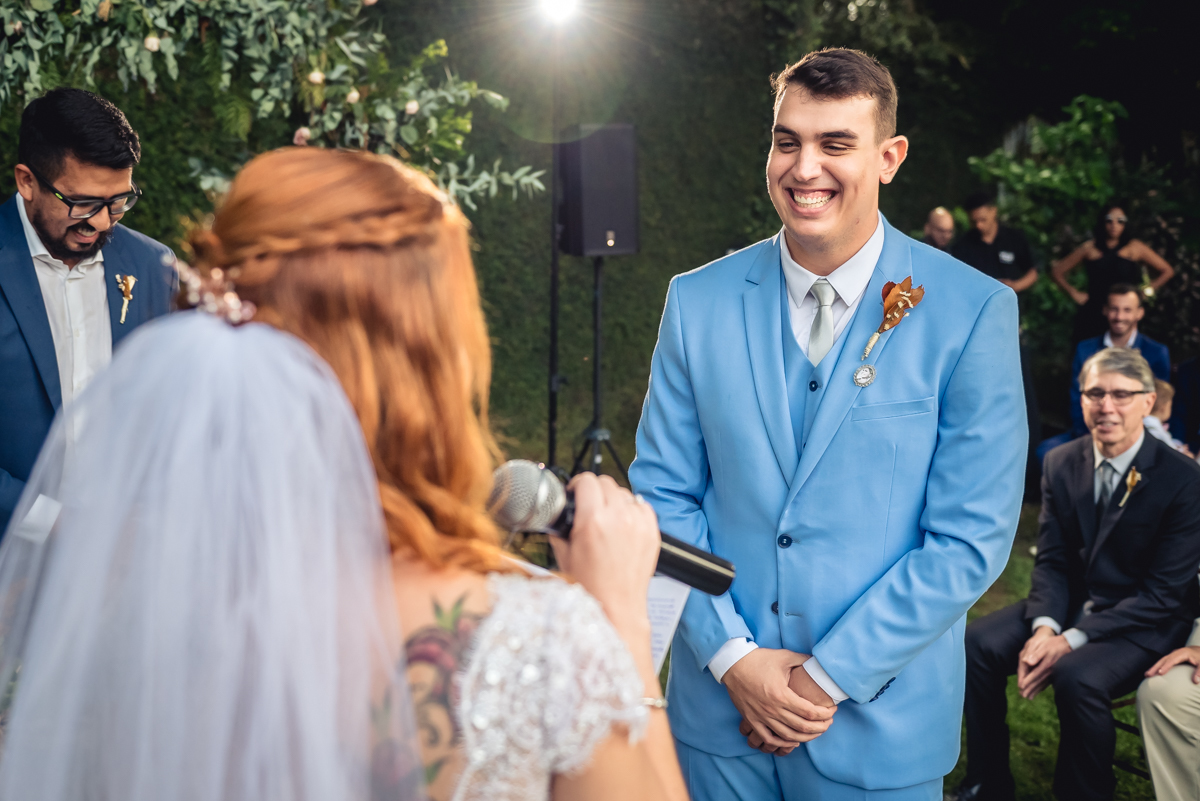 noivo sorri durante os votos realizados pela noiva durante a celebração do casamento de dia ao fim da tarde no sitio da paz na barra da Tijuca - RJ