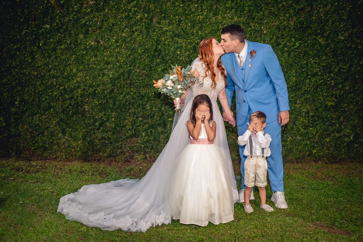noivos se beijando com pajem e daminha no casamento no campo na barra da Tijuca - RJ