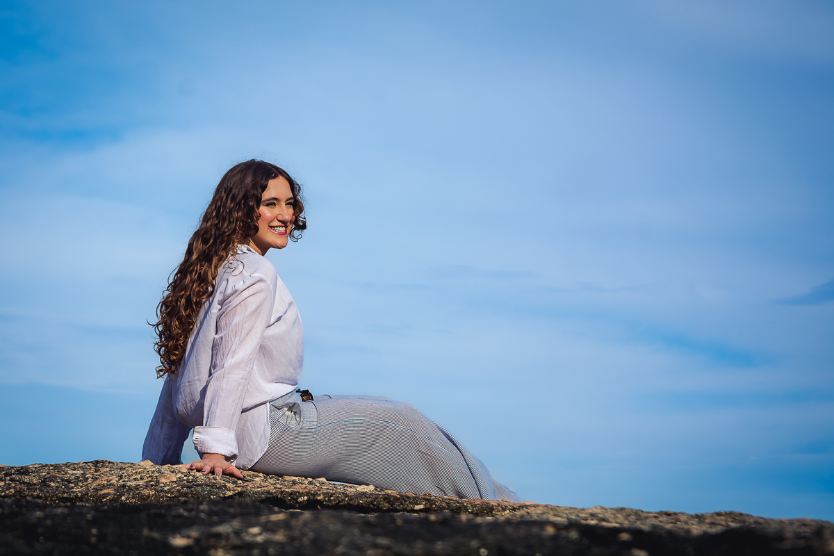 Debutante sentada na pedra, em Itacoatiara, com o céu azul ao fundo 
