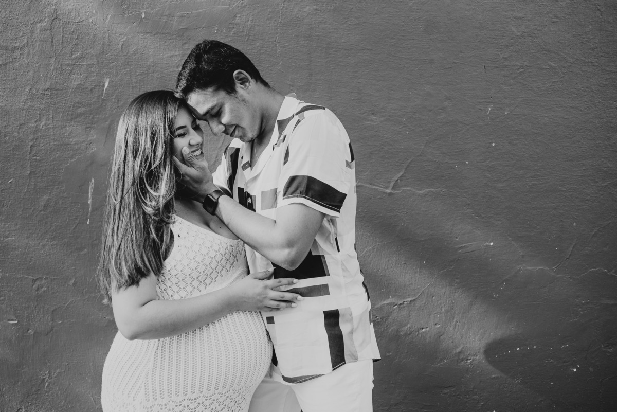 Foto de casal esperando seu primeiro filho, o pai acaricia o rosto da mamãe enquanto sorriam.