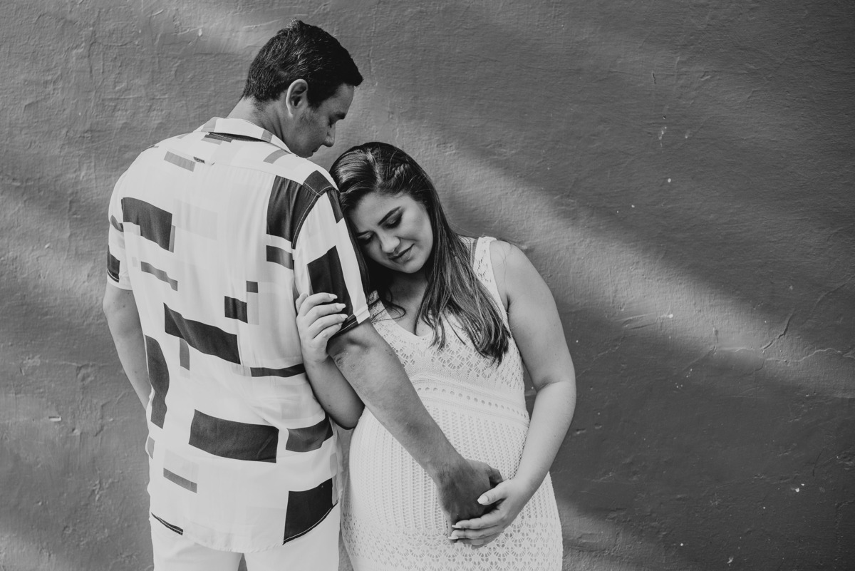 Foto de casal esperando seu primeiro filho, a mamãe deita sob o ombro do papai e acaricia seu bebe. 