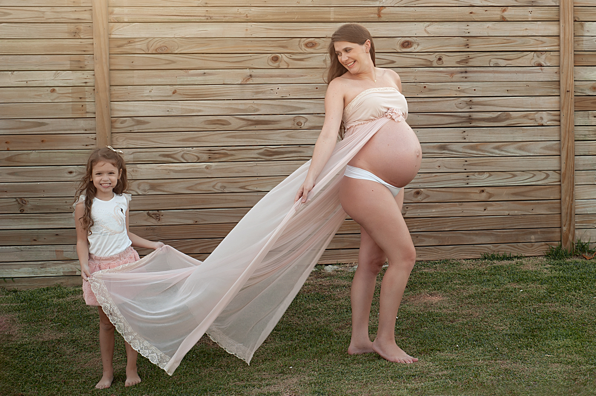 Mae e filha durante o ensaio gestante a menina segurando o vestido da mamãe 