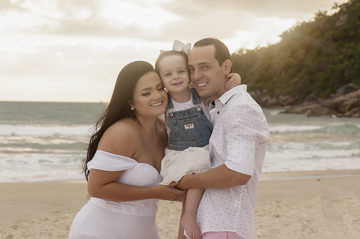 Jovem casal com a filhinha no colo sorrindo na Praia Brava