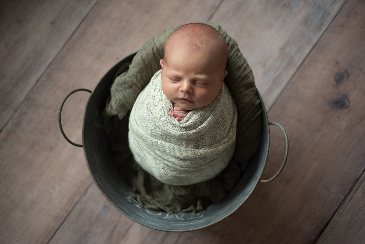 Bebê lindo recém-nascido deitado no baldinho enroladinho no wrap