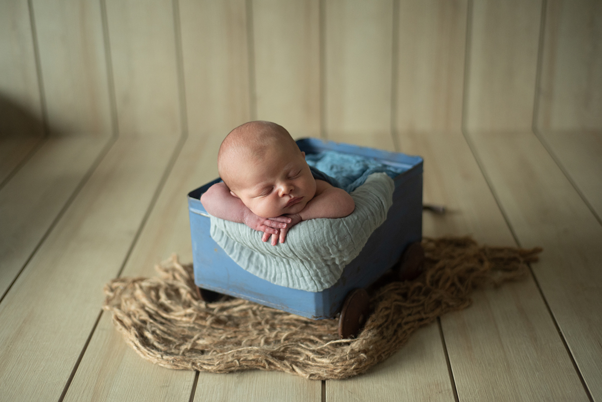 Newborn lindo gordinho na pose de bracinho no carrinho vintage azul da Love Prop