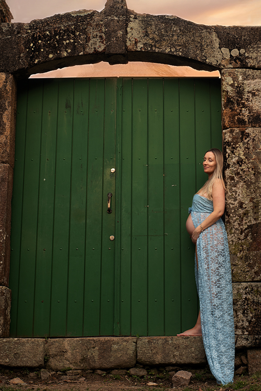 Grávida de vestido azul na porta verde de madeira no Forte de Pedras em Florianópolis