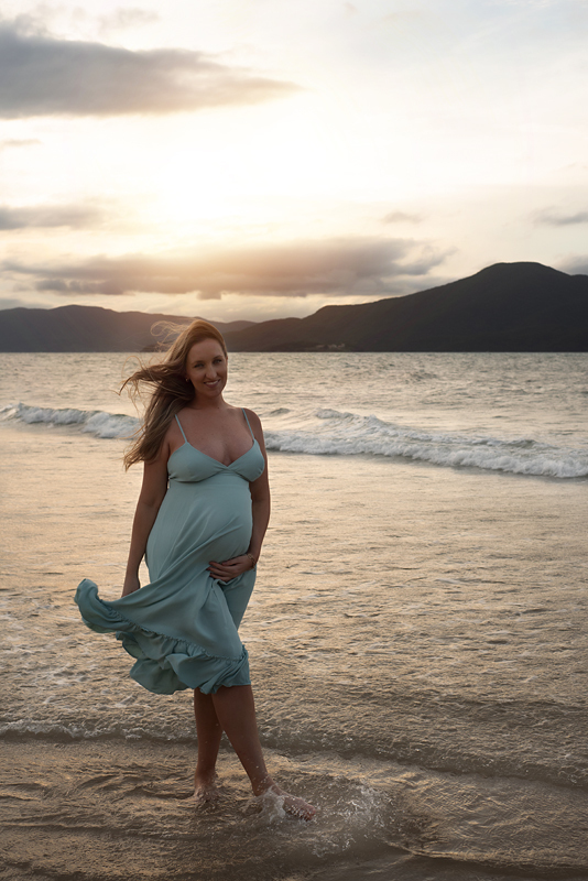 Grávida de vestido verde caminhando na Praia do Forte fotografada por Claudia Milani