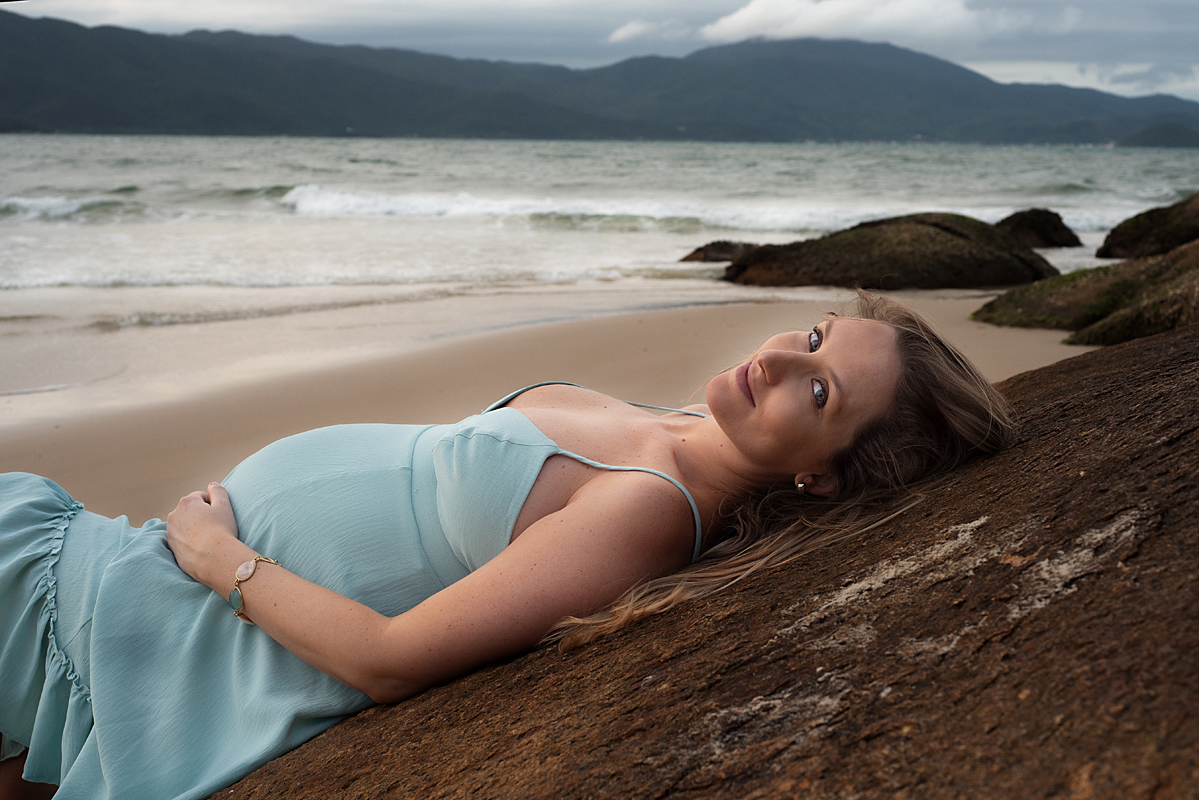 Marília de vestido verde deitada na pedra na Praia do Forte fotografada por Claudia Milani
