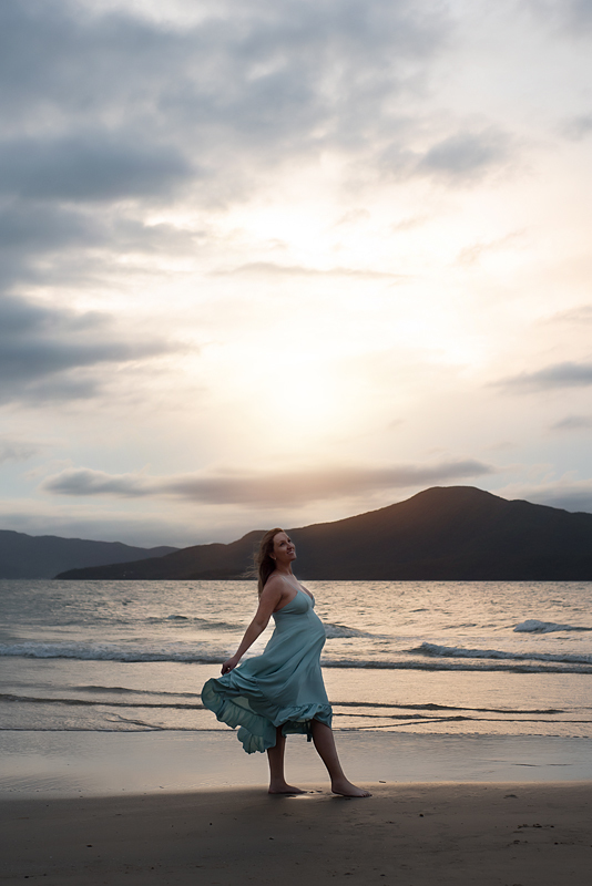 Grávida de vestido verde vendo por do sol na Praia do Forte fotografada por Claudia Milani