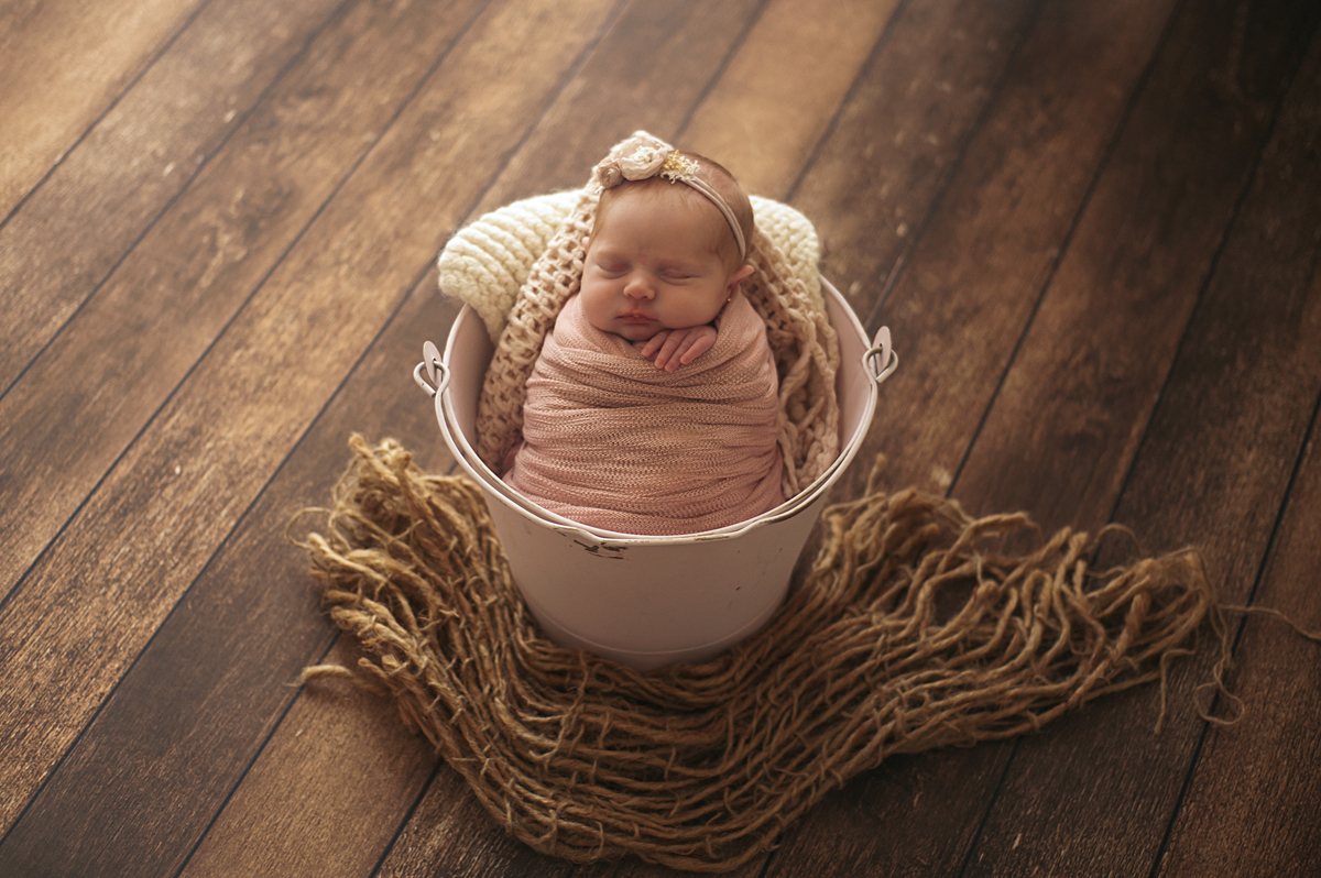Bebê newborn no baldinho basic rosa sobre o fundo amadeirado e burlap layer marrom
