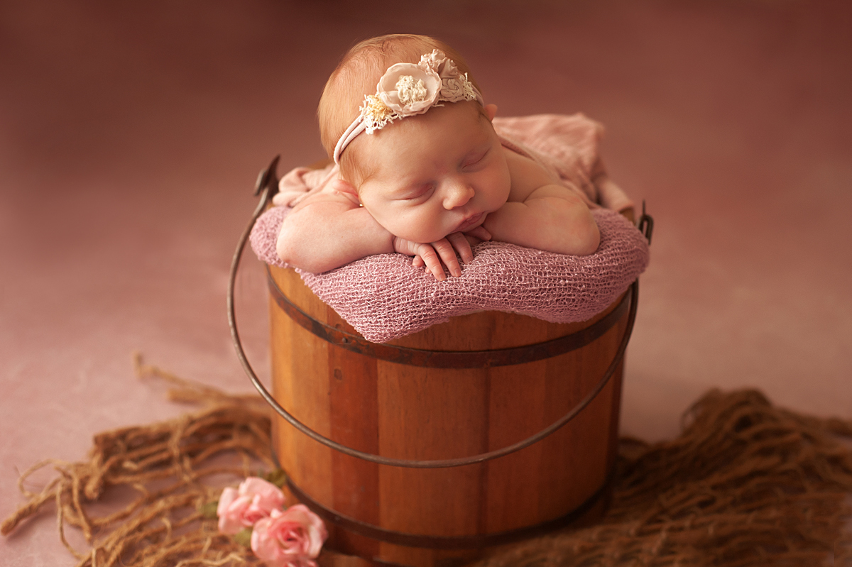 Newborn no baldinho de madeira usando headband e burlap layer