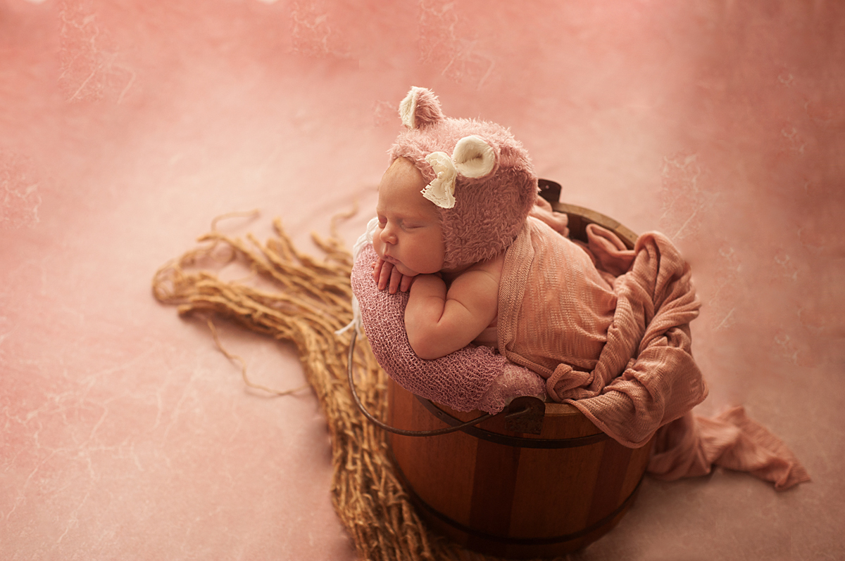 Bebê com touca de ursinho rosa no balde de madeira