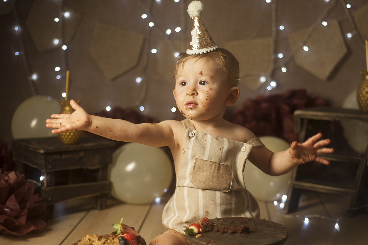 Bebê de braços abertos usando roupa neutra e chapeu com o número 1