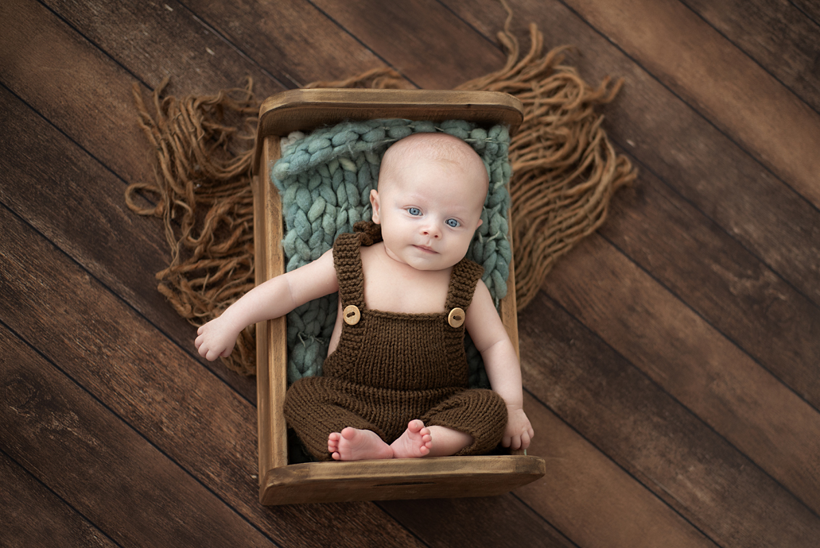 Bebê no ensaio de 2 meses deitado na caixinha usando roupa de tricô marrom