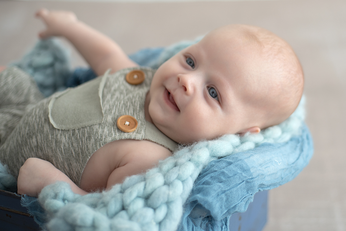 Bebê lindo de olhos azuis sorrindo no ensaio de acompanhamento de 2 meses