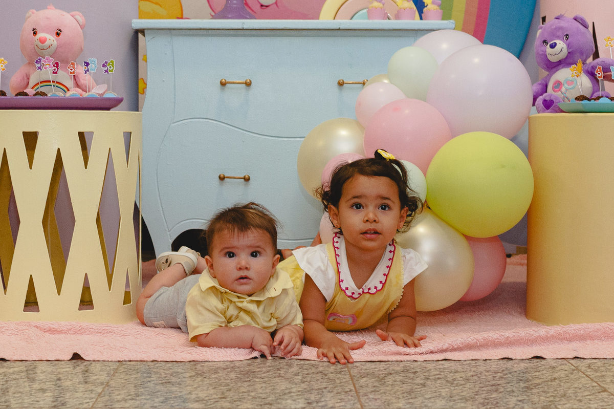 Menina e bebê deitados de bruços na frente da mesa do bolo