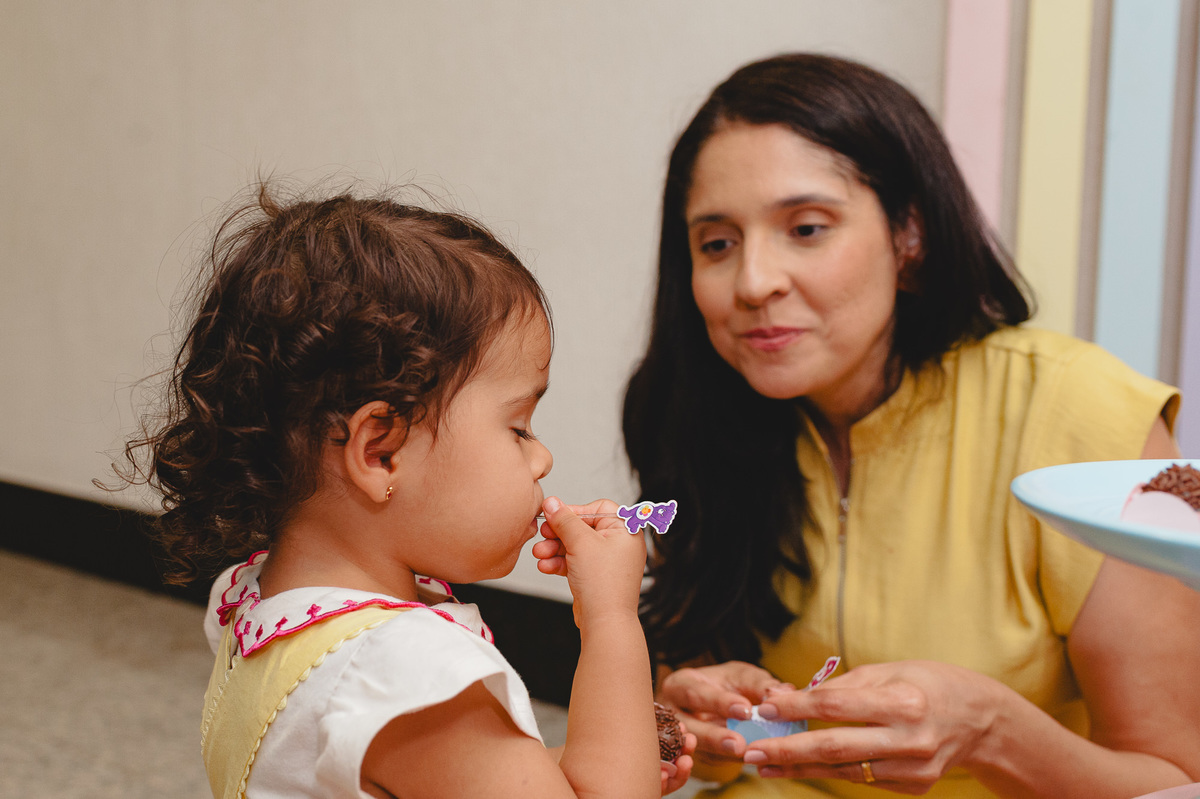 Menina comendo brigadeiro e mãe contemplando