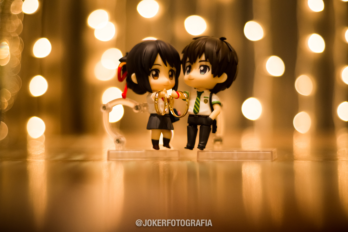 noivos que gostam de anime usam bonecos do filme your name para foto das alianças com inspiração geek