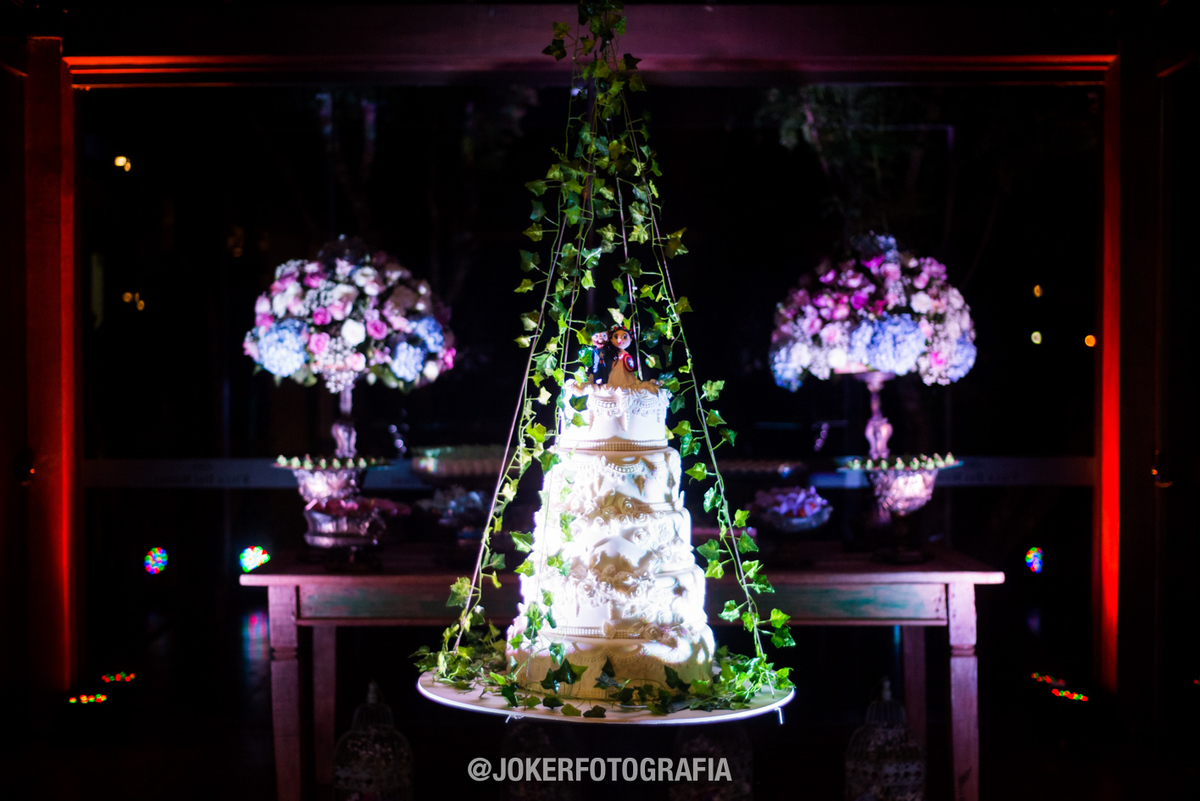 Mesa de doces com bolo suspenso e iluminação cênica para casamento