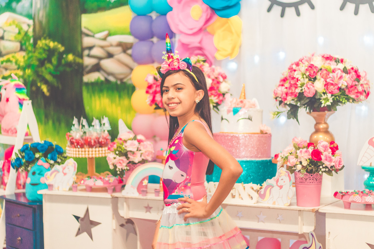 Foto de aniversariante em frente a decoração de festa infantil com tema de unicórnio