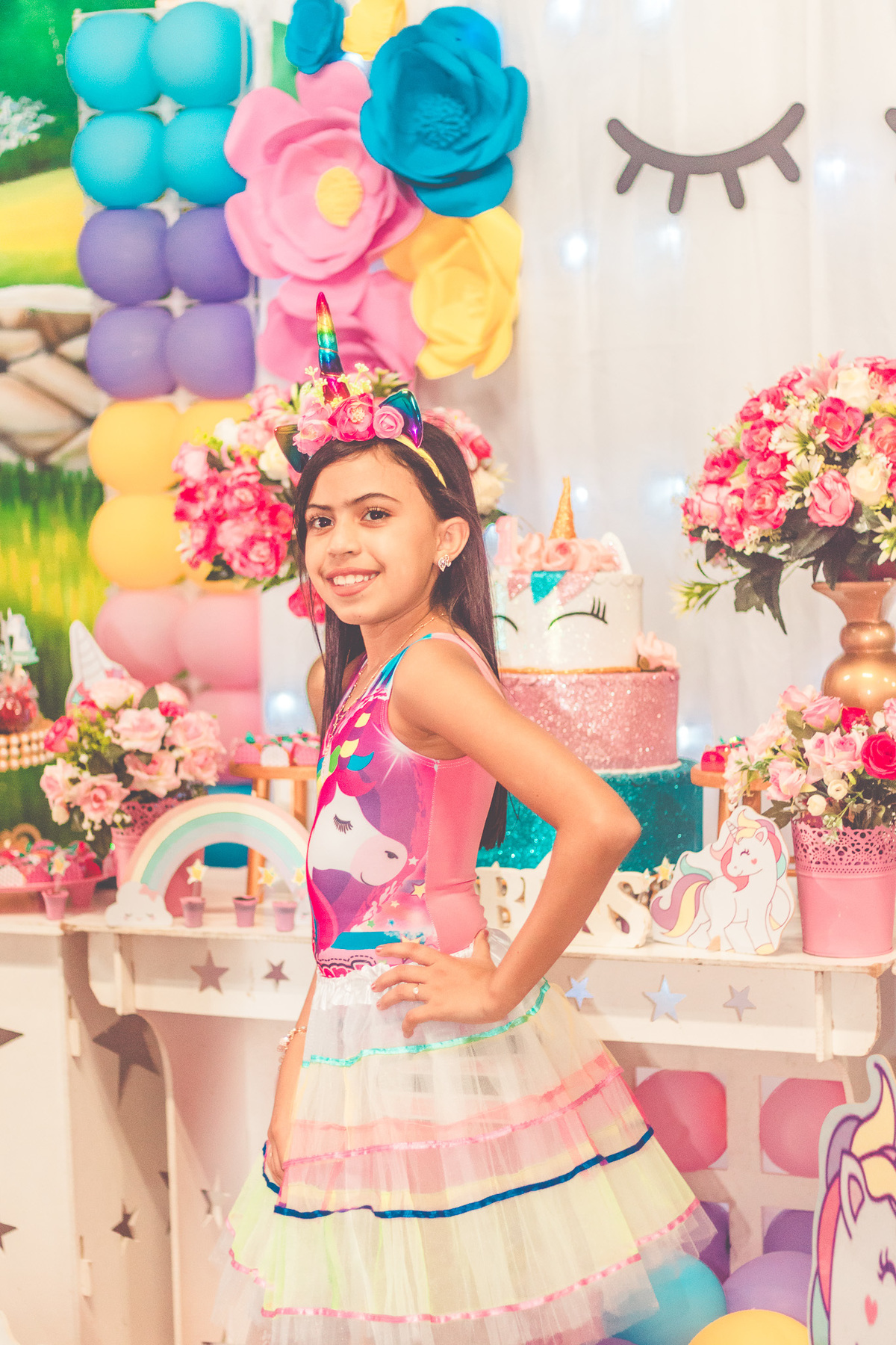 Foto de aniversariante em frente a decoração de festa infantil com tema de unicórnio