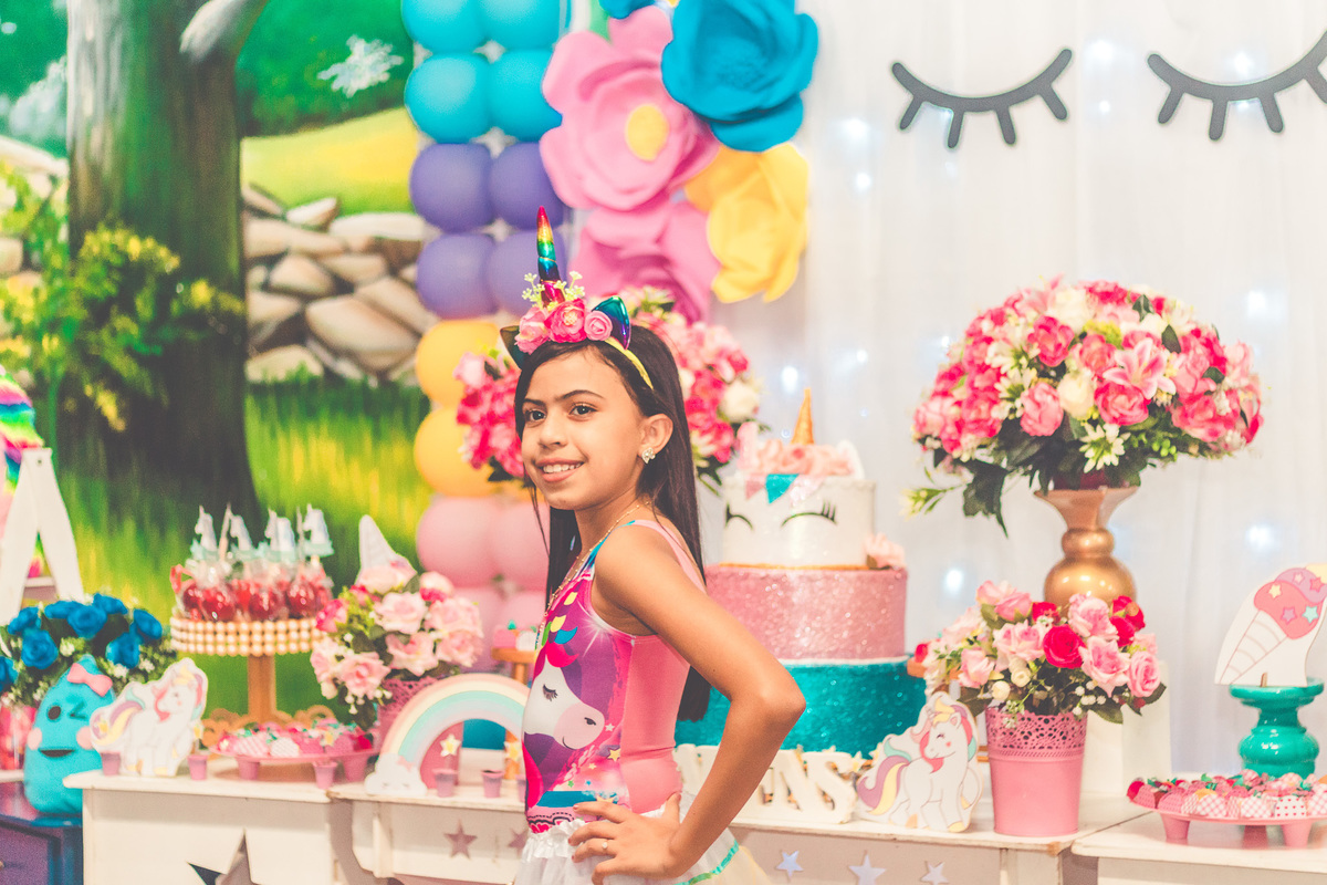 Foto de aniversariante em frente a decoração de festa infantil com tema de unicórnio