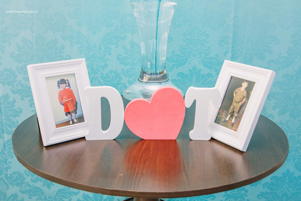Fotos dos noivos da infancia na entrada da festa em cima de uma mesinha e bem ao meio as iniciais deles
