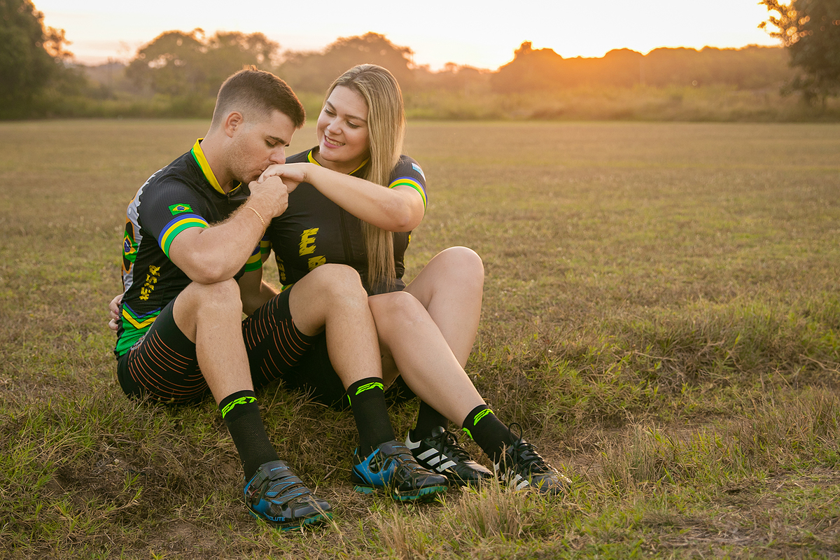 Casal sentado em campo verde em ensaio pré-casamento em Santo Antônio de Pádua, no Rio de Janeiro, com noivo beijando a mão da noiva