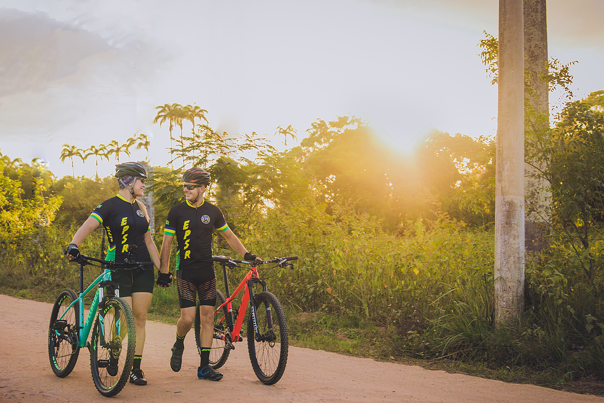 casal empurrando suas bicicletas em campo verde durante ensaio pré casamento no por do sol em santo antonio de pádua no rio de janeiro