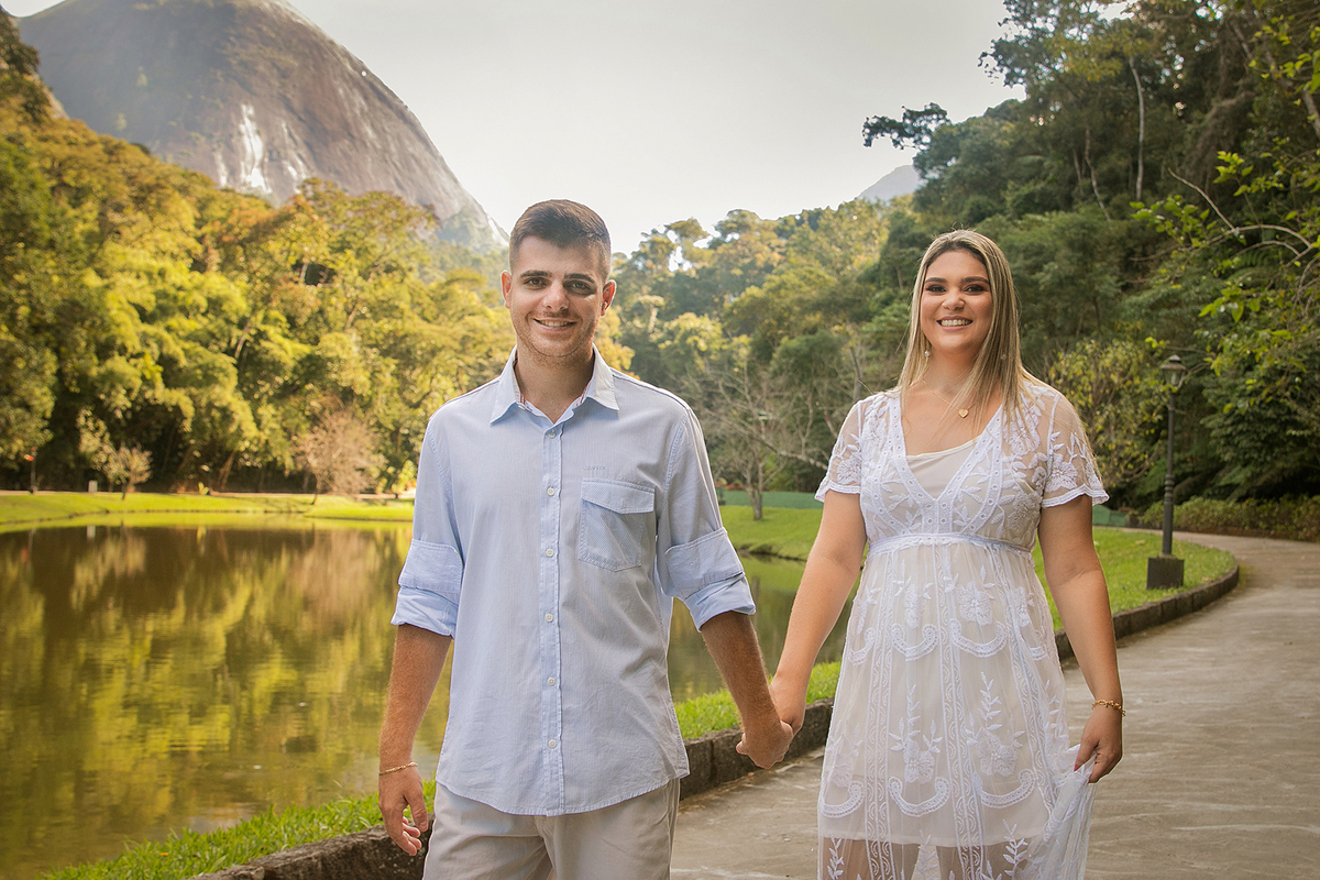 Casal de mãos dadas com roupas claras perto de um lago e uma montanha em seu ensaio pre casamento em Country Club em Nova Friburgo no rio de janeiro