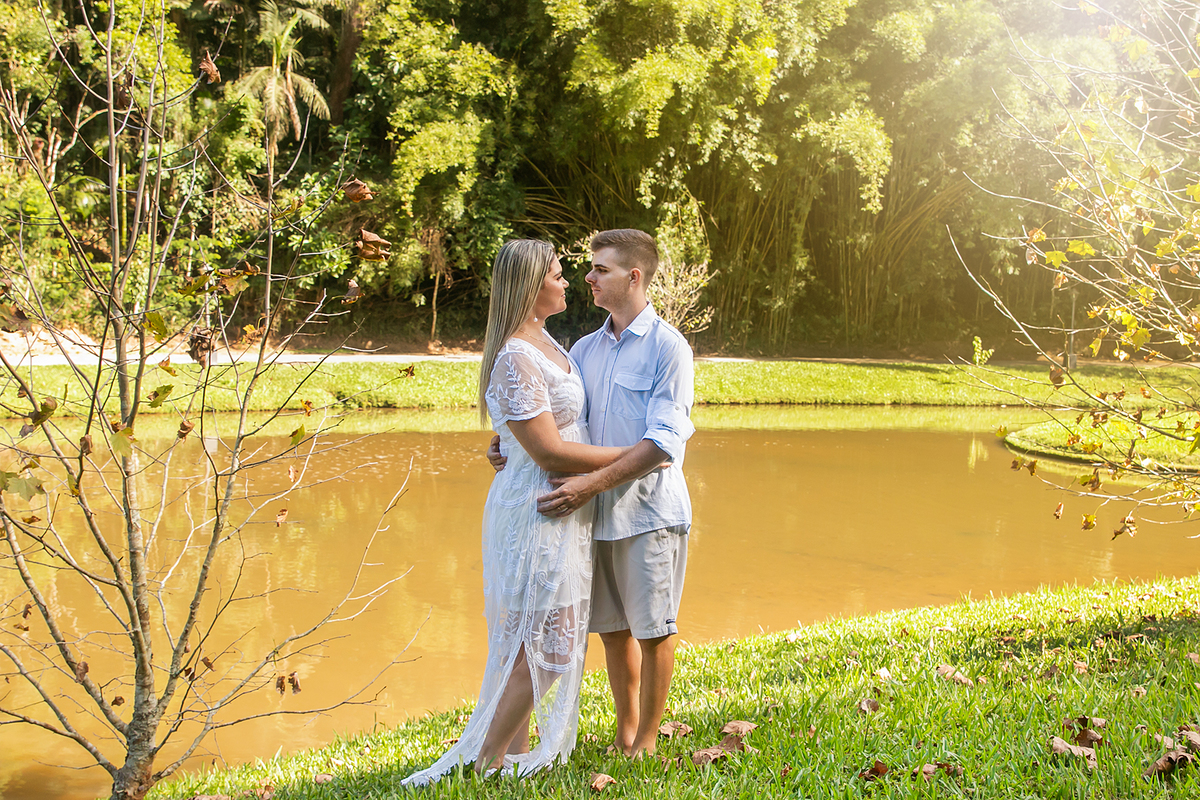 Casal abraçados com roupas claras perto de uma lago com raios de sol em seu ensaio pre wedding no Country Club em Nova Friburgo no rio de janeiro